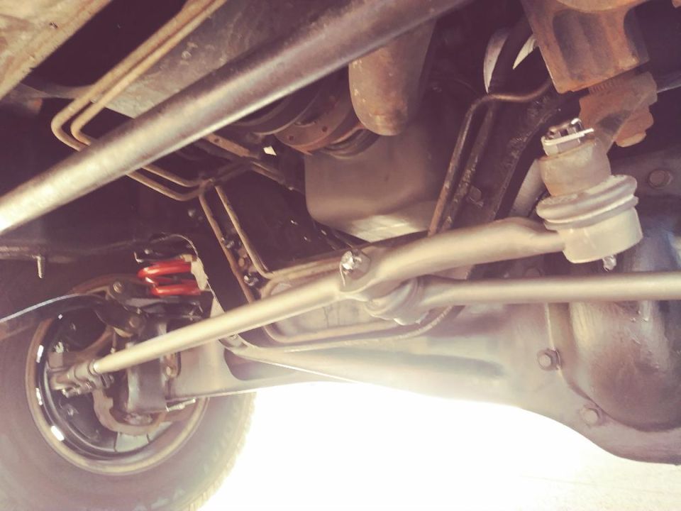 Underside of a vehicle showing suspension components, steering linkage, red coil springs, wheel, and differential.