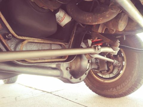 1996 Ford Bronco - Underside view of a vehicle's front axle and suspension components, including the differential, tie rod, and a red coil spring. A BFGoodric…
