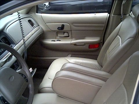 1999 Ford Crown Victoria - The interior of a car is shown, tan leather seats and door panels.
