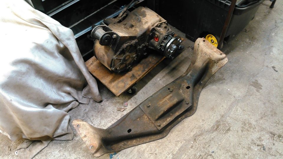 Dirty transfer case on a dolly with a rusty crossmember and cloth.