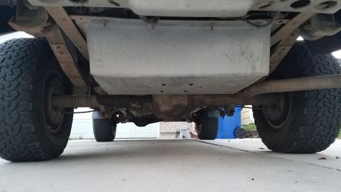 1985 Ford Bronco - The underside of a vehicle, likely a truck or SUV, showing the rear axle, leaf springs, exhaust pipe, and a skid plate protecting the fuel…