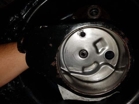 1978 Ford Bronco - A gloved hand is holding a black metal automotive part, revealing a shiny, circular interior with three holes. The exterior of the part sho…