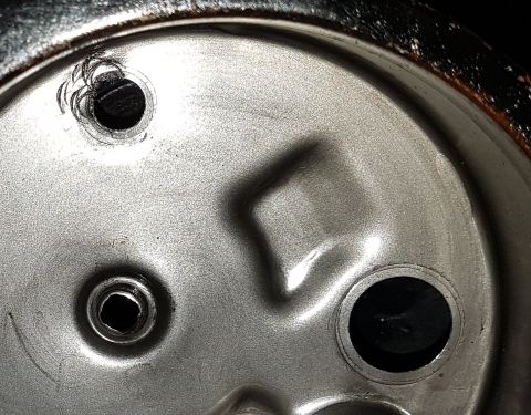 1978 Ford Bronco - The underside of a metal can lid shows two circular holes. One hole has a jagged edge from being opened, and the other appears to be a manu…