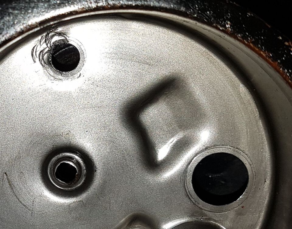 Underside of a metal can lid with two holes, one jagged.