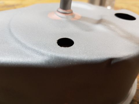 1978 Ford Bronco - A close-up, low-angle shot of a gray metal part with two circular holes and a central shaft. The part appears to be dented in several place…