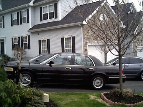 1999 Ford Crown Victoria - A black sedan with chrome accents is parked in front of a residential building.