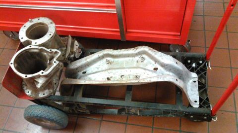 1978 Ford Bronco - Two aluminum transmission bell housings and a silver metal crossmember are loaded onto a red and black dolly. The parts are positioned in f…