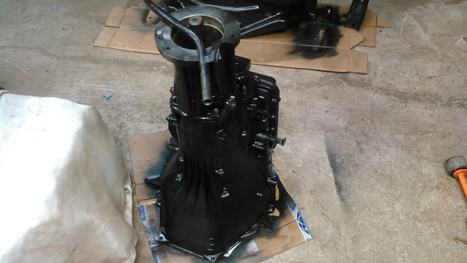 Black painted transmission on cardboard with white tarp to the side.