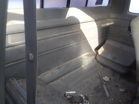 1994 Ford Bronco - The interior of a vehicle's cabin shows a dirty floor with scattered debris and broken glass. A gray seatbelt is visible on the left side o…