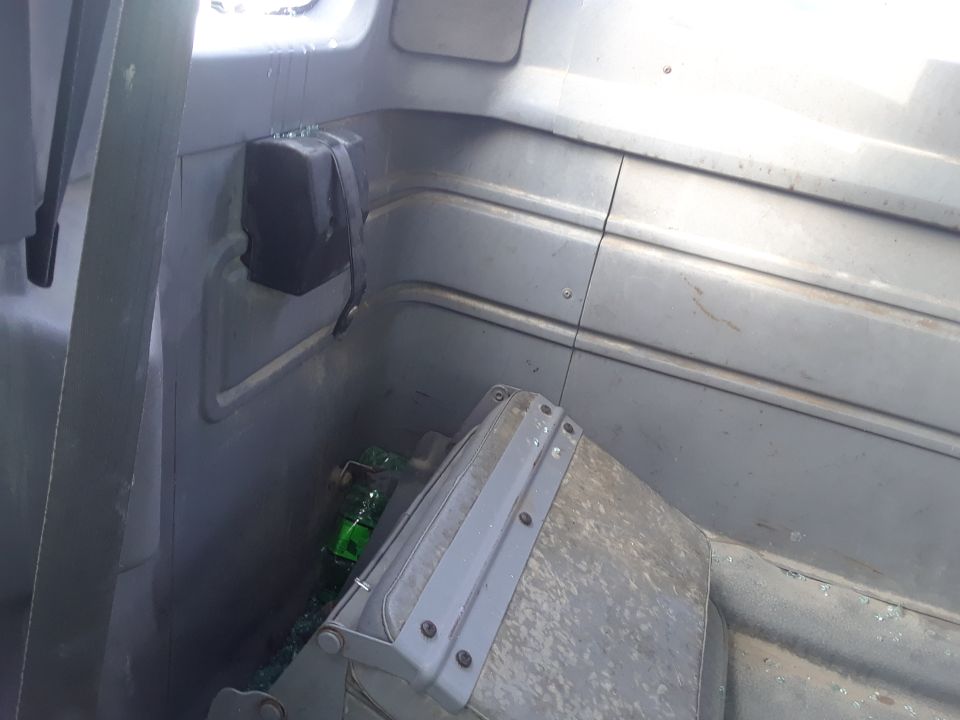 Interior of a gray vehicle with a broken green bottle and a black storage compartment.