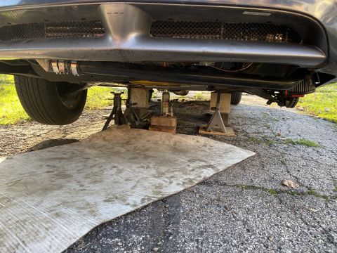 Underside of a car on jack stands, with plywood on driveway.