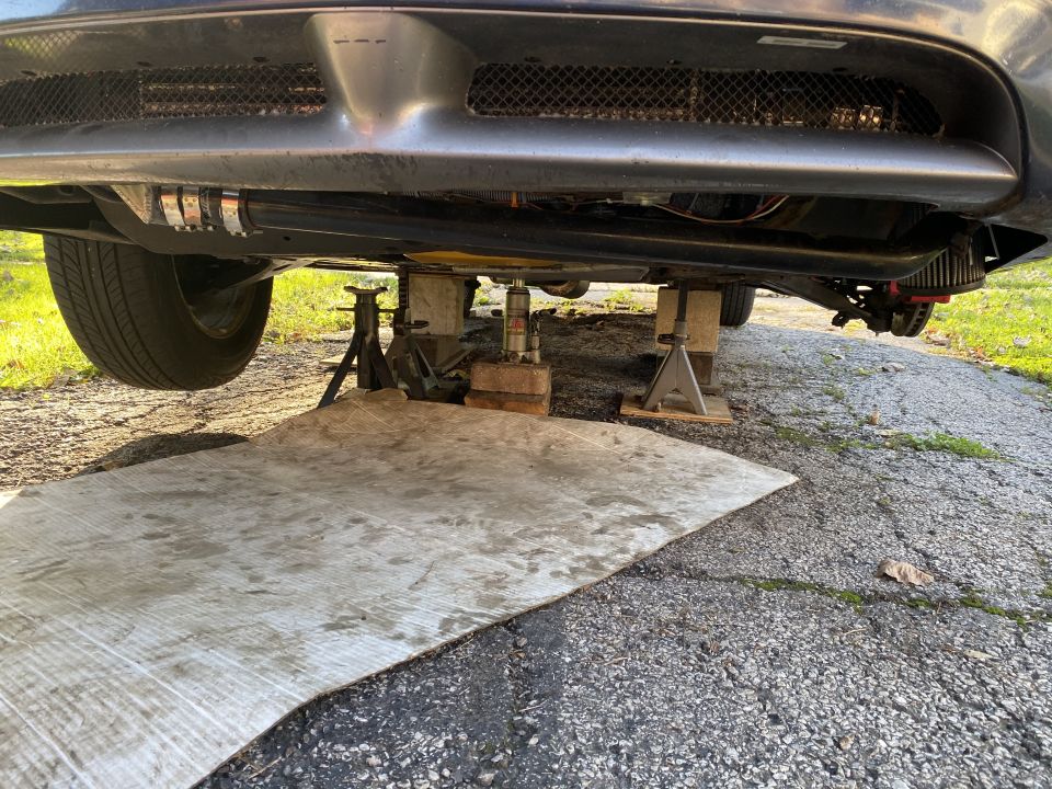 Underside of a car on jack stands, with plywood on driveway.