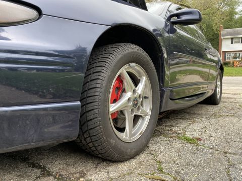 Dark blue 2000 Pontiac Grand Prix driver's side front wheel and fender with red brake calipers.
