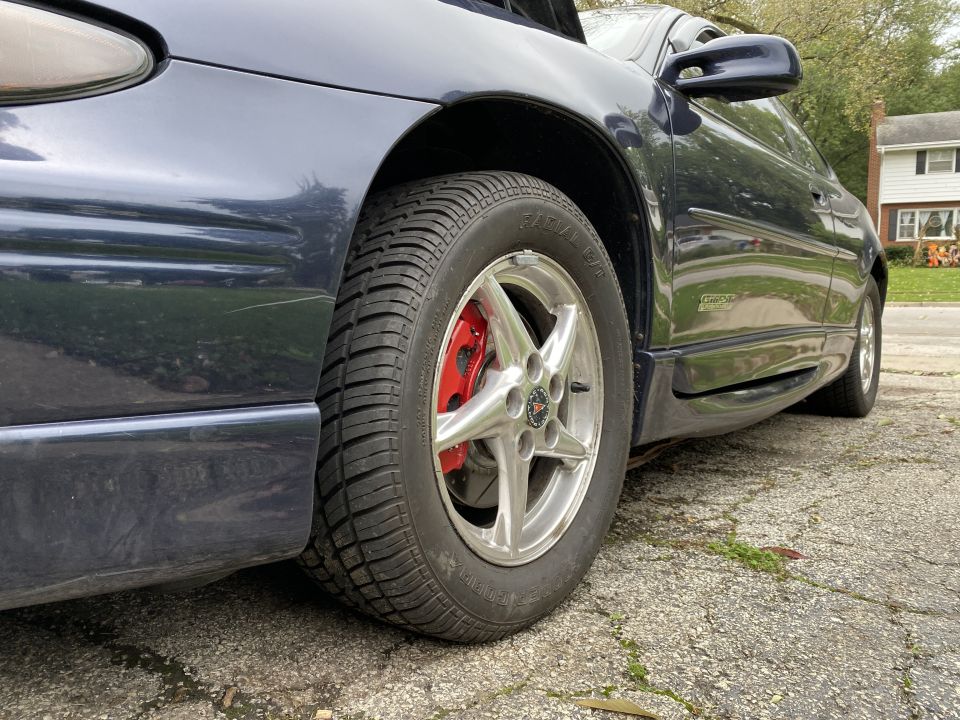 Dark blue 2000 Pontiac Grand Prix driver's side front wheel and fender with red brake calipers.