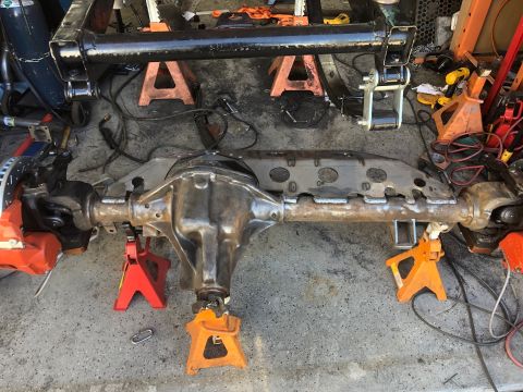 1992 Jeep Wrangler - A heavy-duty rear axle assembly, likely from a Jeep Wrangler, is mounted on jack stands on a concrete floor. The axle features a custom-fab…