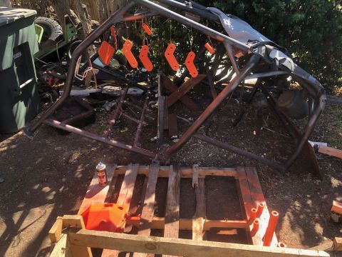 1992 Jeep Wrangler - A collection of orange-painted metal parts hang from a metal frame outdoors, with a spray can and a painted orange component on a wooden pa…