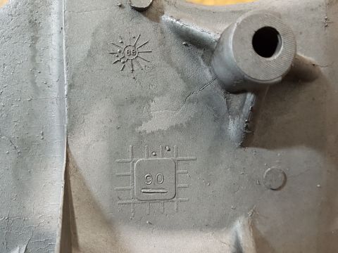 1978 Ford Bronco - A close-up view of a gray metal casting with embossed markings. Visible text includes '89' within a sunburst pattern and '90' within a squa…