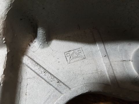 1978 Ford Bronco - A close-up view of a cast metal part with a stamped logo that appears to be a triangle with a 'P' and 'A' inside. There is also some faint,…