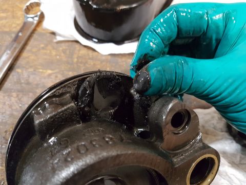 1978 Ford Bronco - A gloved hand is shown inspecting a heavily greased, black metal automotive part with visible damage to its rim. A wrench is visible in the…
