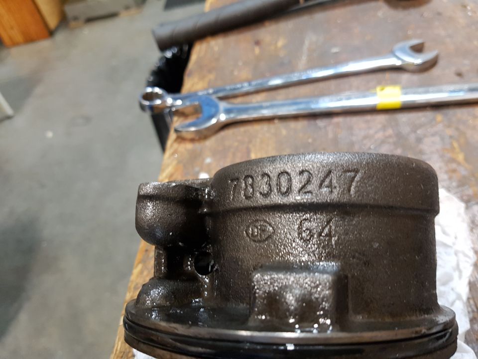 Metal part with numbers 7830247 and 64 stamped on it, on a workbench with wrenches.