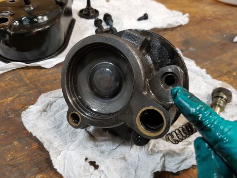 1978 Ford Bronco - A gloved hand points to a disassembled brake master cylinder assembly, resting on a white cloth on a wooden workbench. Other parts of the a…