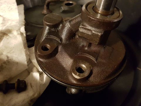 1978 Ford Bronco - A close-up, angled view shows a dark brown, oily power steering pump with a metal shaft protruding from the top. Two threaded holes are vis…
