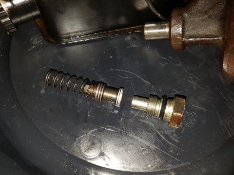 1978 Ford Bronco - A disassembled hydraulic valve with a spring and plunger assembly is laid out on a dark surface, possibly a drip pan.