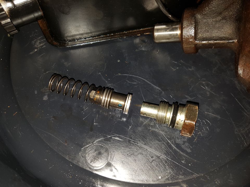 Disassembled hydraulic valve with spring and plunger on a dark surface.