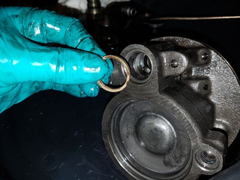 1978 Ford Bronco - A gloved hand holds a small, circular metal ring over a section of a greasy, metallic automotive part. The part appears to be a housing wit…