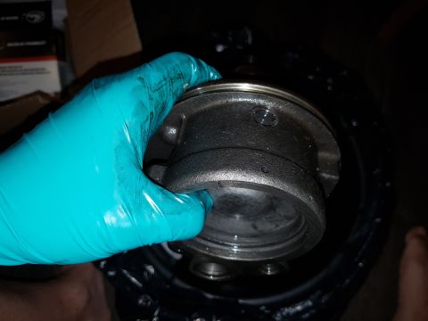 1978 Ford Bronco - A gloved hand holds a metal automotive part, possibly a hub or bearing assembly, over a dark container. The part is dark gray and shows som…