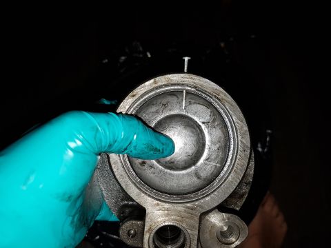 1978 Ford Bronco - A gloved hand points into a metal component, possibly an oil filter housing or a similar engine part. The component has a circular opening…
