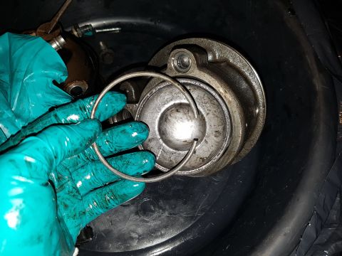 1978 Ford Bronco - A person wearing teal gloves holds a metal retaining ring over a disassembled metal component, likely part of a vehicle's engine or drivetr…