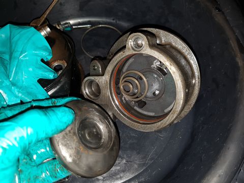 1978 Ford Bronco - A gloved hand holds a metal component over a disassembled engine part with visible springs and an orange seal.