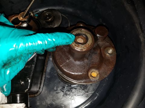 1978 Ford Bronco - A gloved hand points to a bearing on a rusty metal component, likely part of a vehicle's engine or drivetrain, submerged in a dark basin.