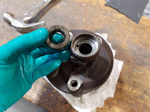 1978 Ford Bronco - A gloved hand holds a metal seal with visible text, positioned above a dark brown metal component with a circular opening. A hammer is visi…