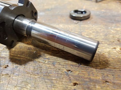 1978 Ford Bronco - A close-up view of a metallic shaft with visible scoring marks, resting on a weathered wooden surface. A black flange is attached to the le…
