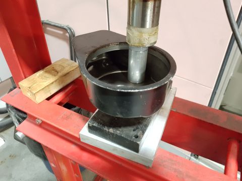 1978 Ford Bronco - A black metal cup is being pressed into a larger black metal object by a silver hydraulic press ram. A wooden block is placed on the red fr…