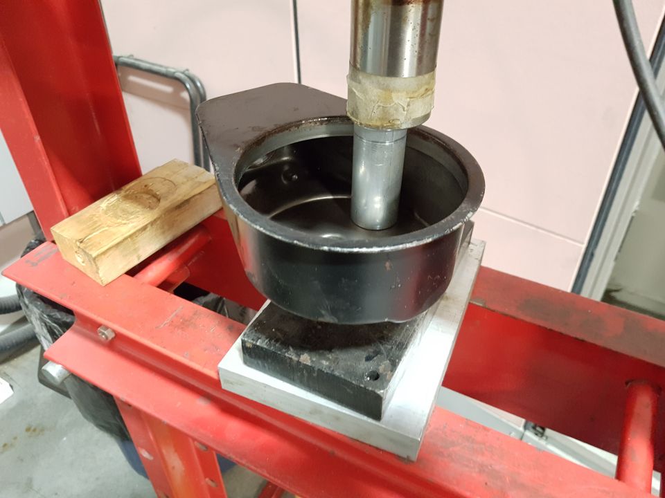 Hydraulic press ram pressing a black cup into another black metal object.