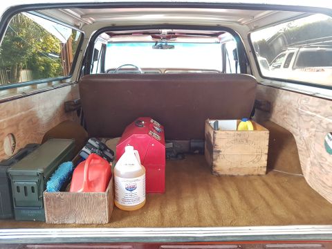1978 Ford Bronco - The cargo area of a vintage Ford Bronco is filled with various items, including ammo cans, a red toolbox, fuel cans, and cleaning supplies.
