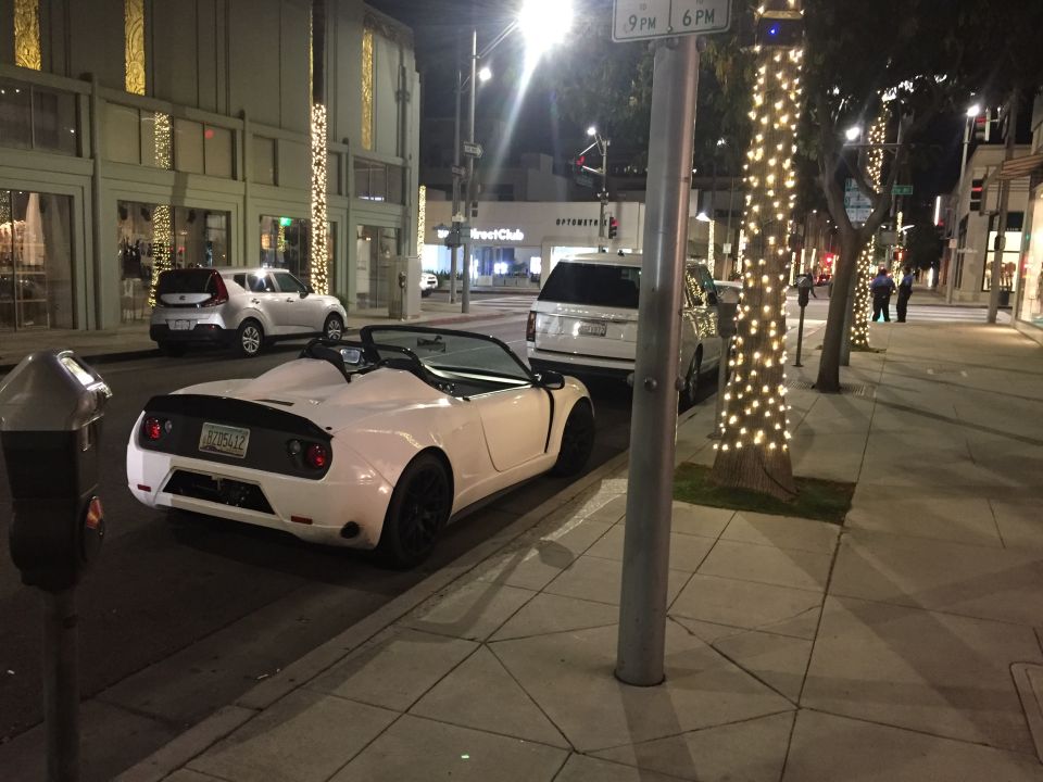 White convertible sports car with black rear accent and California license plate BZD5412 parked on city street at night.