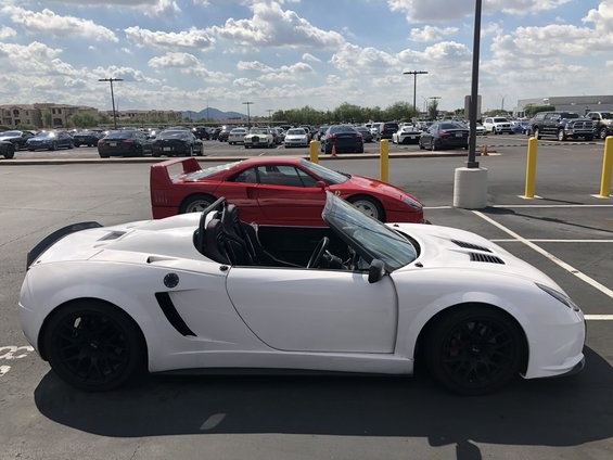 White sports car with driver's door open, red sports car underneath, parked in a lot.