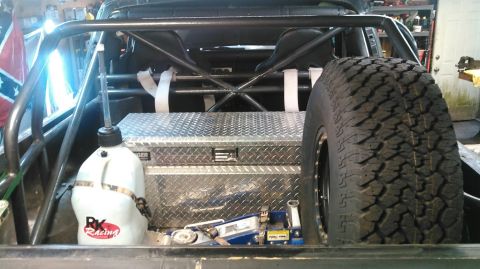 1978 Ford Bronco - The interior of a modified vehicle shows a roll cage, racing seats, a diamond plate toolbox, a spare tire, a fuel jug, and a hydraulic jack.