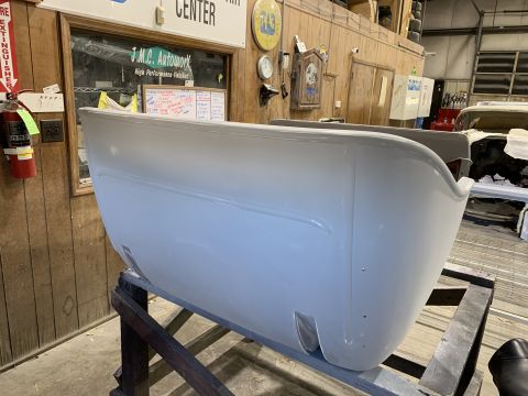 1923 Ford Model T - A light gray, unfinished vehicle body, possibly a car fender or tub, is mounted on a wooden stand in what appears to be an auto repair shop…