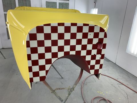 1923 Ford Model T - A yellow car fender is shown with a red and white checkerboard pattern applied to the side. The part is mounted on a stand in what appears…