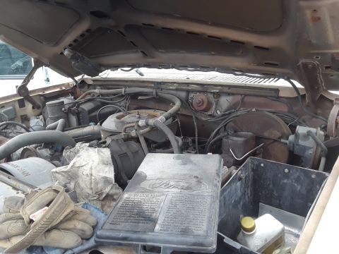 1994 Ford Bronco - The open hood of a vehicle reveals a dusty and somewhat rusty engine bay. A black plastic air cleaner housing with a Ford logo is prominent…