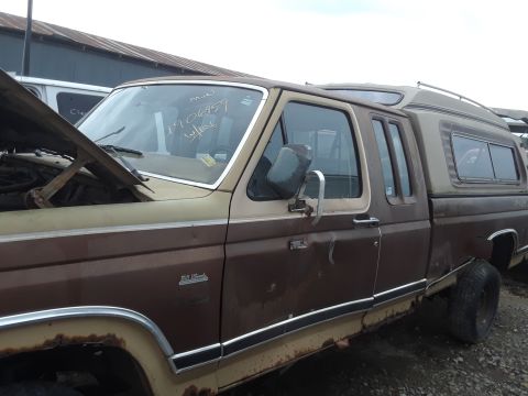 1994 Ford Bronco - A brown and tan two-door pickup truck with a camper shell is parked outdoors. The hood is open, revealing the engine compartment, and there…