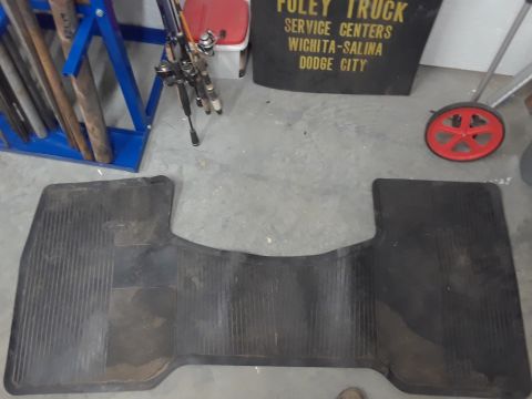 1994 Ford Bronco - A black rubber floor mat with a ribbed pattern is laid out on a concrete floor. The mat has a distinctive shape that suggests it is for a v…