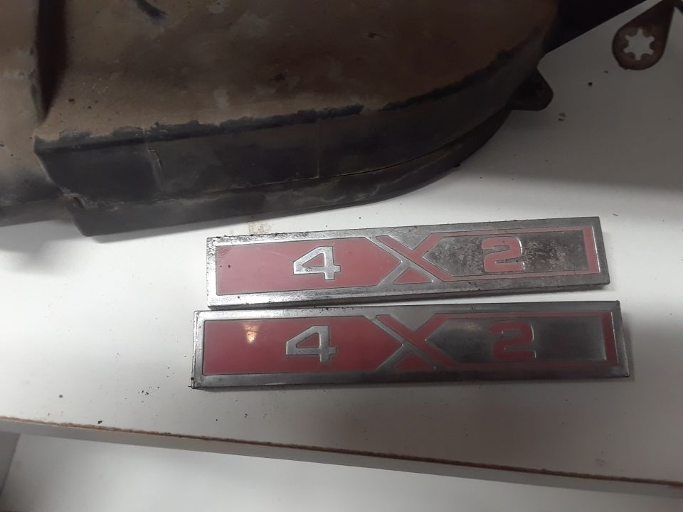 Two 4X2 emblems on a white surface with a dark vehicle part in the background.