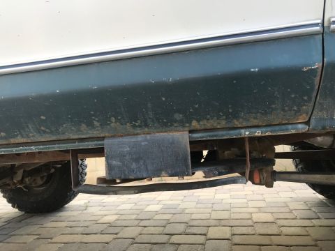1979 Ford Bronco - A close-up side view of the lower body and undercarriage of a dark green and white vehicle, possibly a 1979 Ford Bronco. Visible modificati…