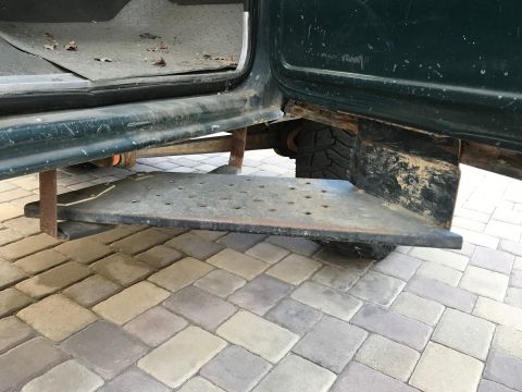 1979 Ford Bronco - A close-up view of the driver's side step and lower door frame of a dark green vehicle, showing wear and tear. The step is made of perforat…